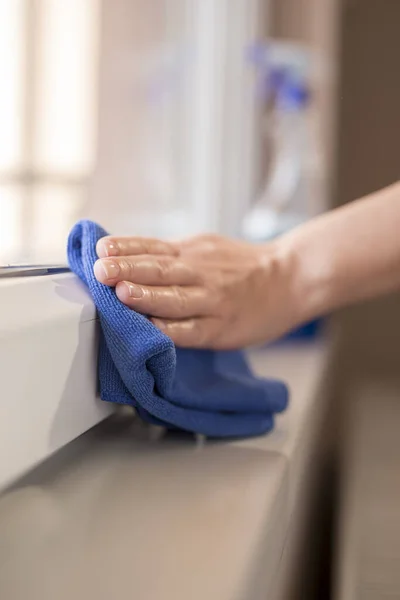 Detail of female hands wiping windows with a cleanser spray and a cloth; housekeeping assistant wiping windows