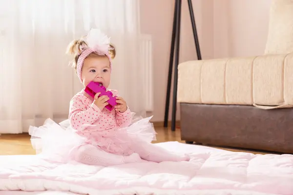 美しい小さな赤ちゃんの少女は ピンクのチュートゥスカートを着て 保育園の床に羽毛布団の上に座って遊んで おもちゃのブロックを噛んで — ストック写真