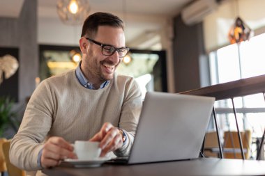Restoran masasında oturan, kahve içen ve dizüstü bilgisayar üzerinde çalışan serbest çalışan bir erkek portresi.