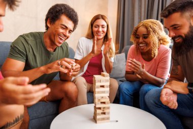 Bir grup neşeli genç arkadaş evde birlikte vakit geçiriyorlar, Jenga oynuyorlar, bir kuleden blokları sırayla kaldırıyorlar ve üstüne istifliyorlar.