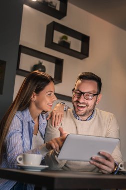 Restoran masasında oturan, kahve içen ve tablet bilgisayarda internette sörf yapan güzel genç bir çift.
