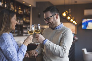 Genç bir çift randevuda, restoranın tezgahının yanında durur, kadeh kaldırır, öğle yemeği için bir masa beklerken kadeh kaldırır.
