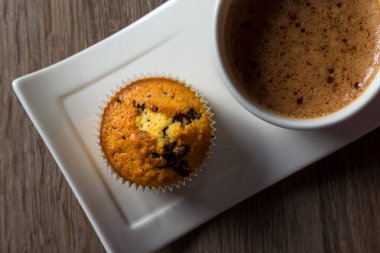 Tabakta bir fincan kahve, çikolatalı mekik, ahşap bir masada kek, üst manzara.