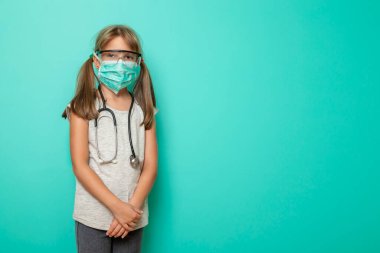 Nane rengi arka planda cerrahi maske, steteskop ve koruyucu laboratuar gözlüğü takan küçük güzel bir kız; çocuk doktoru ya da hemşireyi canlandırıyor.