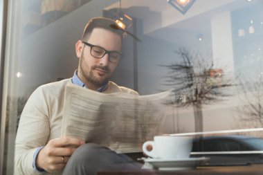 Restoran masasında oturmuş gazete okuyup kahve içen düşünceli bir adamın portresi.