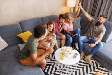 Bir grup arkadaşın evde oyun oynayıp zaferi kutlarken yüksek açılı görüntüsü.