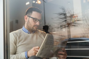 Restoran masasında oturmuş gazete okuyup kahve içen düşünceli bir adamın portresi.