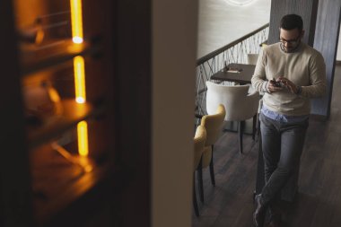 Yakışıklı bir adam restoranda duruyor, akıllı bir telefona mesaj yazıyor.