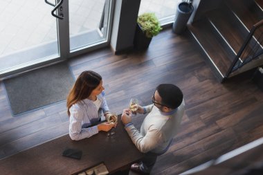 Genç bir çiftin randevudaki yüksek açılı görüntüsü. Restoran tezgahının yanında durmuş, şarap içip sohbet ediyorlar.