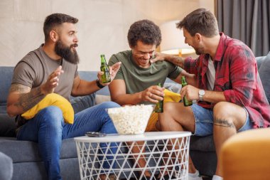 Bir grup erkek evde vakit geçirip, televizyon izleyip, patlamış mısır yiyip, bira içerek eğleniyor.