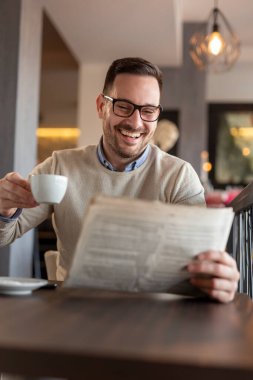 Restoran masasında oturan, gazete okuyan ve kahve içen bir adam.