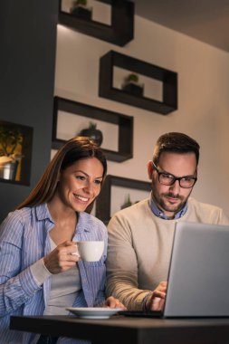 Restoran masasında oturan, kahve içen ve dizüstü bilgisayar kullanan bir çift.