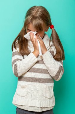 Grip olan küçük bir kızın portresi. Nane rengi arka planda kağıt mendillerle burun sümkürme ve silme.