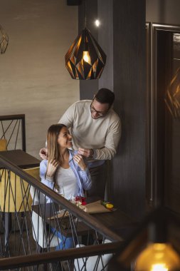 Restoranda doğum gününü kutlayan genç ve güzel bir çift kadının boynuna kolye takan bir adam.