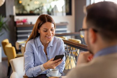 Genç bir kadın restoranda randevudayken akıllı telefon kullanıyor ve mesaj yazıyor.