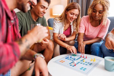 Bir grup neşeli genç arkadaş evde birlikte vakit geçirirken Ludo masası oyunu oynayarak eğleniyorlar.