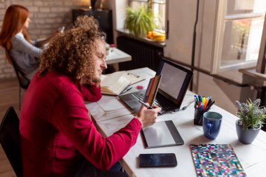 Modern ofiste çalışan erkek tasarımcı, bir renk paletinden bir renk seçer; birlikte çalışan serbest çalışanlar