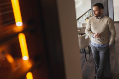 Yakışıklı bir adam restoranda duruyor, gözlüklerini tutuyor ve mesafeye bakıyor, düşünceli.