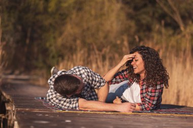 Çiftler göl kenarı pikniğinde eğleniyor piknik örtüsüne uzanıyor ve doğada güzel bir sonbahar gününün tadını çıkarıyor.
