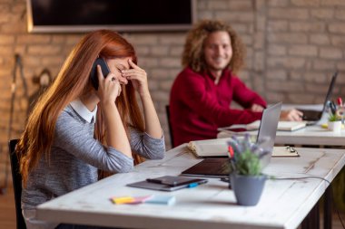 Modern bir ofiste çalışan iş adamları, dizüstü bilgisayarda çalışan bir erkek ile telefon görüşmesi yapan kadınlar, birlikte çalışan serbest çalışanlar.