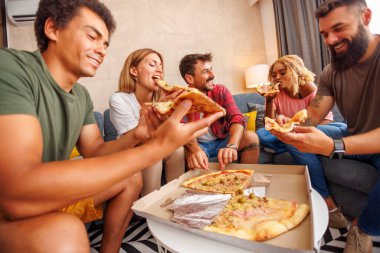 Bir grup arkadaşın kanepede oturup pizza yemesi ve evde birlikte vakit geçirmeleri düşük açılı bir bakış açısı.