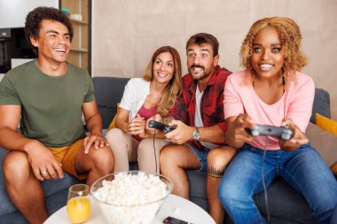 Bir grup neşeli genç arkadaş evde boş zamanlarını geçirirken video oyunları oynayarak eğleniyorlar.