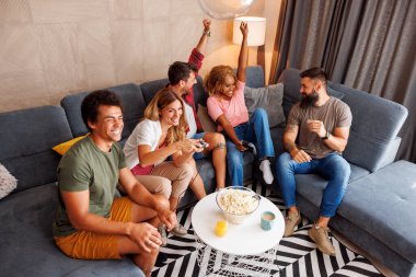 Bir grup arkadaşın evde oyun oynayıp zaferi kutlarken yüksek açılı görüntüsü.