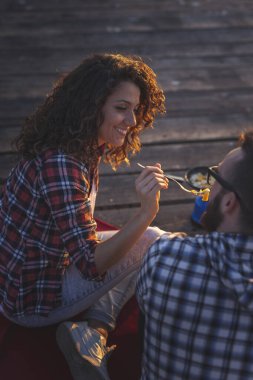 Rıhtımda kamp yapan, yemek yiyen ve günbatımının keyfini çıkaran bir çiftin yüksek açılı görüntüsü.