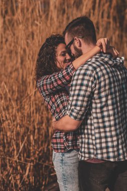 Güzel genç çift dışarıda eğleniyor, güneşli bir günü doğada geçiriyor, göl rıhtımlarında sarılıp öpüşüyor.