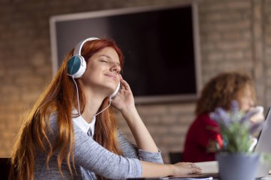 Üniversitenin okuma odasında müzik dinlerken dinlenen, ders çalışmaya ara vermiş güzel bir genç kız öğrenci.