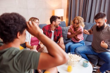 Bir grup neşeli genç arkadaş kelime tahmin oyunu oynarken akıllı telefon uygulaması kullanarak evde vakit geçiriyorlar.