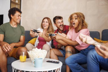 Bir grup neşeli genç arkadaş evde boş zamanlarını geçirirken video oyunları oynayarak eğleniyorlar.