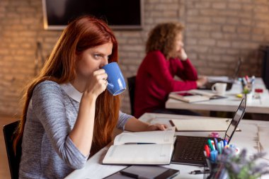 Modern bir ofiste çalışan iş adamları, birlikte çalışan serbest çalışanlar, ofis masasında otururken kahve içen kadınlar.