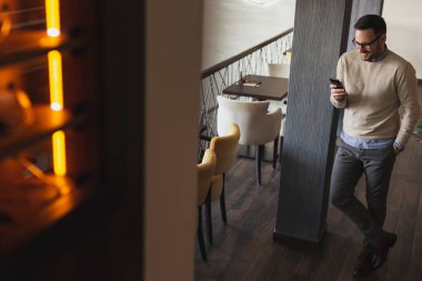 Yakışıklı bir adam restoranda duruyor, akıllı bir telefona mesaj yazıyor.