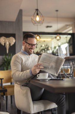 Restoran masasında oturan, gazete okuyup kahve içen bir adam.