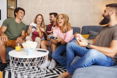 Bir grup neşeli genç arkadaş evde boş zamanlarını geçirirken video oyunları oynayarak eğleniyorlar.