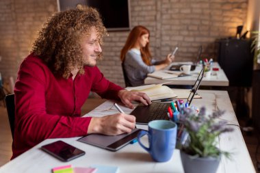 Modern ofiste çalışan erkek tasarımcı, çizim tahtası kullanarak çizim yapıyor; iş yerinde çalışan serbest çalışanlar