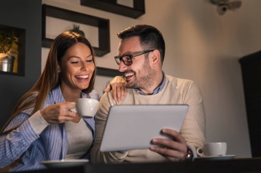Restoran masasında oturan, kahve içen ve tablet bilgisayarda video görüşmesi yapan genç ve güzel bir çift.
