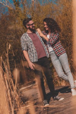 Aşık bir çift göl kenarında yürüyüş yapıyor, doğada güneşli güzel bir günün tadını çıkarıyor; göl rıhtımlarında yürüyen, dışarıda vakit geçiren bir çift.