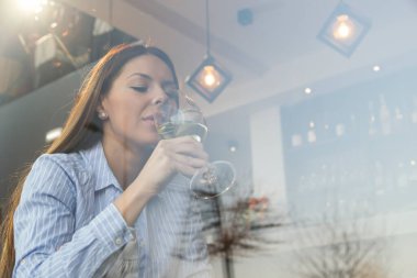 Restoran masasında oturmuş pencereden dışarı bakıp şarap içen güzel bir kadının portresi.