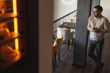 Yakışıklı adam restoranda duruyor, akıllı telefon kullanıyor.