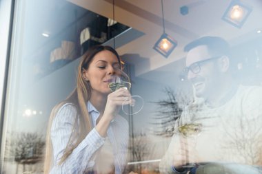 Randevudaki genç bir çiftin portresi. Lokanta masasında oturmuş şarap içiyorlar.