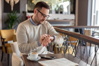 Restoran masasında oturan adam, saatine bakıyor, geç kalan birini bekliyor.