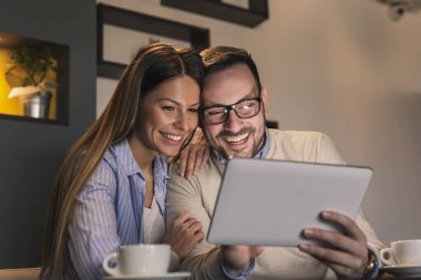 Restoran masasında oturan, kahve içen ve tablet bilgisayar kullanarak video görüşmesi yapan genç ve güzel bir çift.