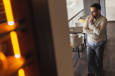 Yakışıklı bir adam restoranda dikiliyor, mesafeye bakıyor, düşünceli ve ciddi.