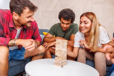 Bir grup neşeli genç arkadaş, evde birlikte vakit geçirirken blok istifleme ve denge oyununu kaldırma oyunu oynayarak eğleniyor.
