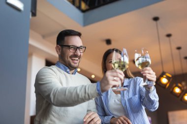 Genç çift bir randevuda, bir restoran tezgahının yanında durmuş, şarap kadehlerini kaldırıyor ve bir masa beklerken kadeh kaldırıyor.
