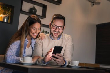 Restoran masasında oturan, kahve içen ve akıllı telefon kullanan genç ve güzel bir çift.