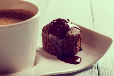 Tabakta bir fincan kahve, çikolatalı mekik, ahşap bir masada kek, üst manzara.