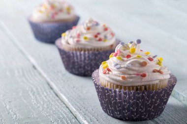 Tahta bir masaya renkli şekerlemeler serpiştirilmiş üç fincan kek. 